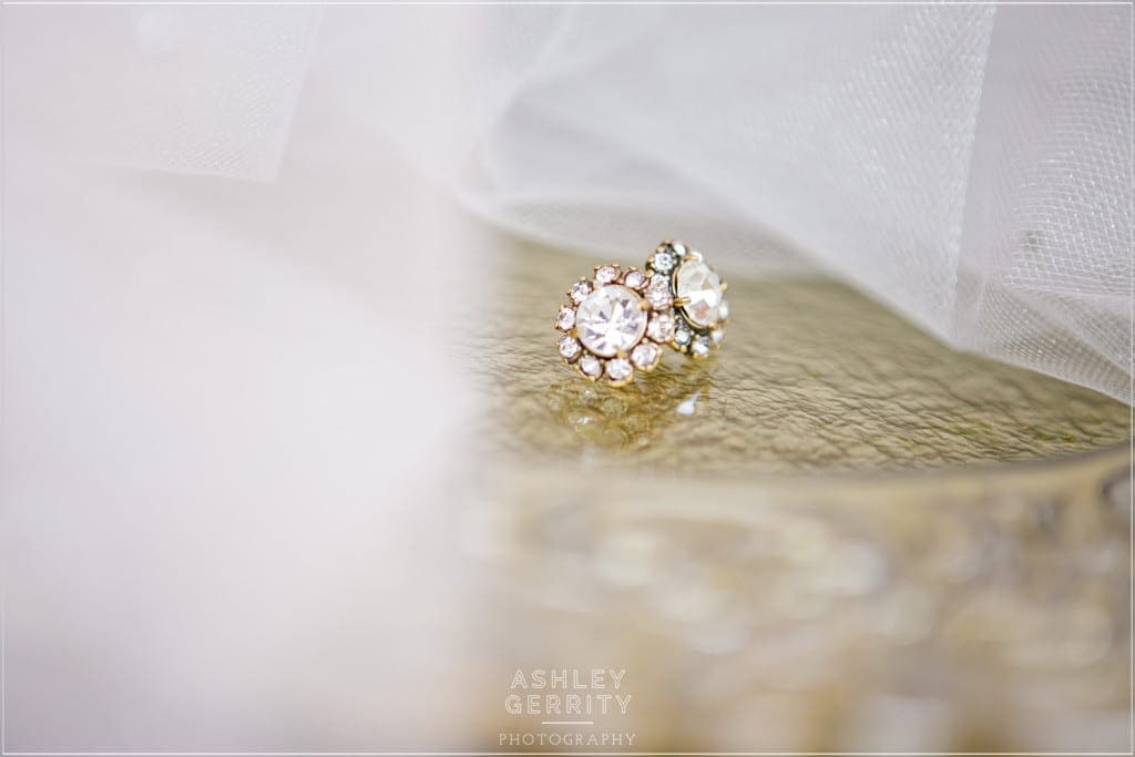 Sparkling J. Crew earrings wrapped in a veil by Romona Keveza in this wedding details photo by Ashley Gerrity Photography.