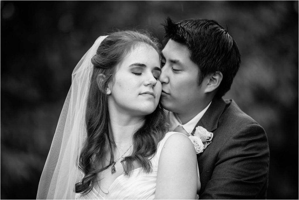 black and white photo groom kissing bride on the cheek