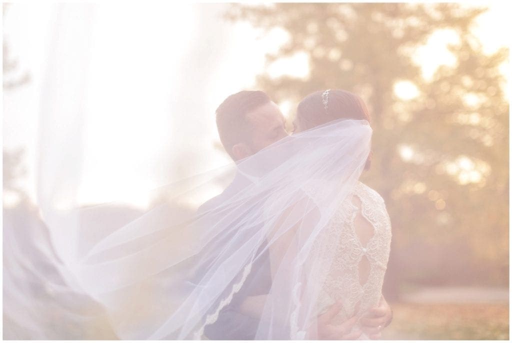 sunset photos of bride kissing groom. I love how the veil is scooping in the sunlight 