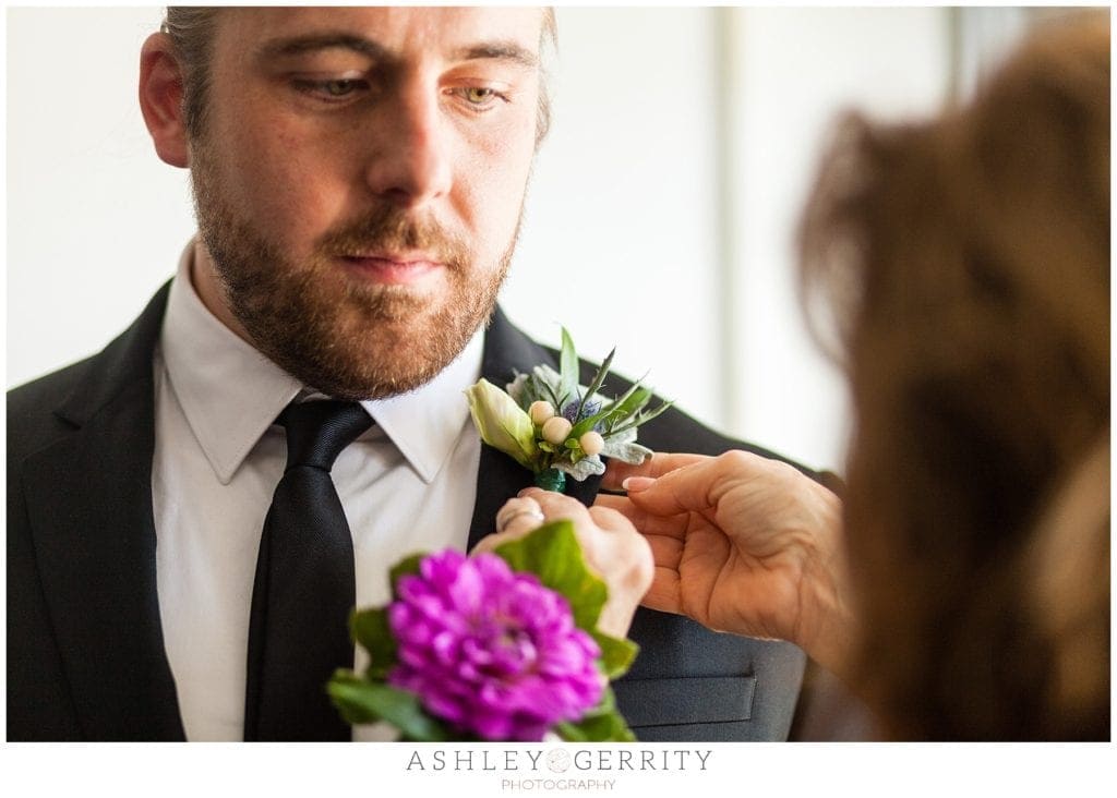 Groom having boutonniere pinned on by mother of the groom