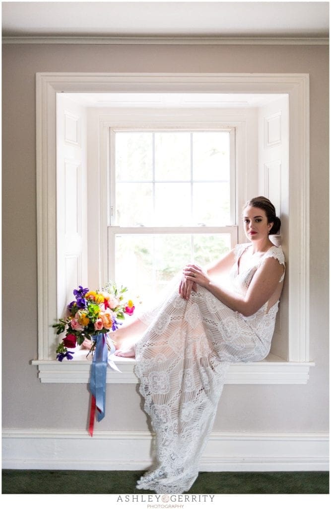 bride in lace Claire pettibone wedding dress posed in window with colorful wildflower bouquet.