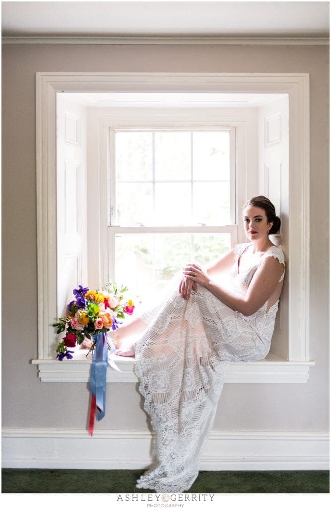 bride in lace Claire pettibone wedding dress posed in window with colorful wildflower bouquet.