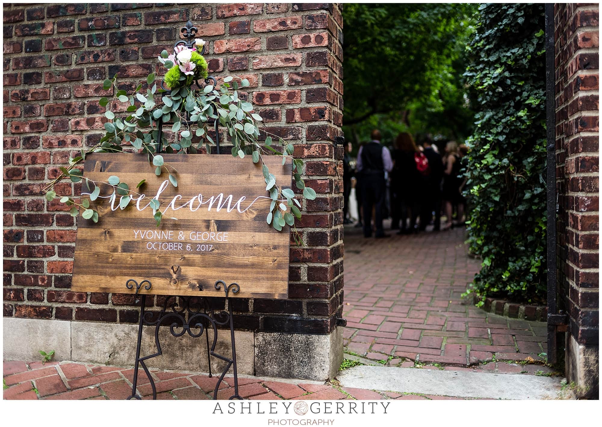 Wooden hand-painted welcome sign was draped with greenery and florals to welcome guests to this Colonial Dames wedding.