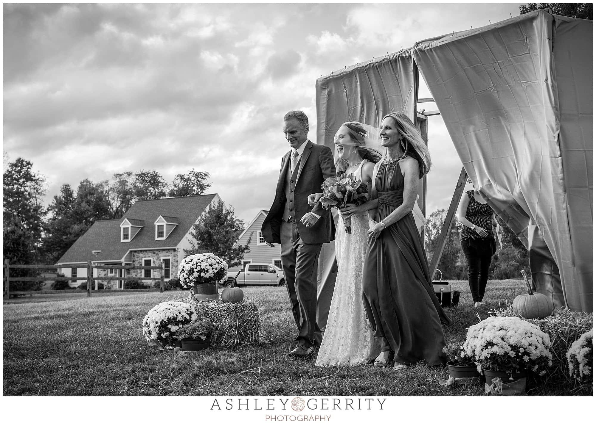 Bride walking down the aisle with her parents for her jewish wedding ceremony, through a flowing drape. Image in black & white.