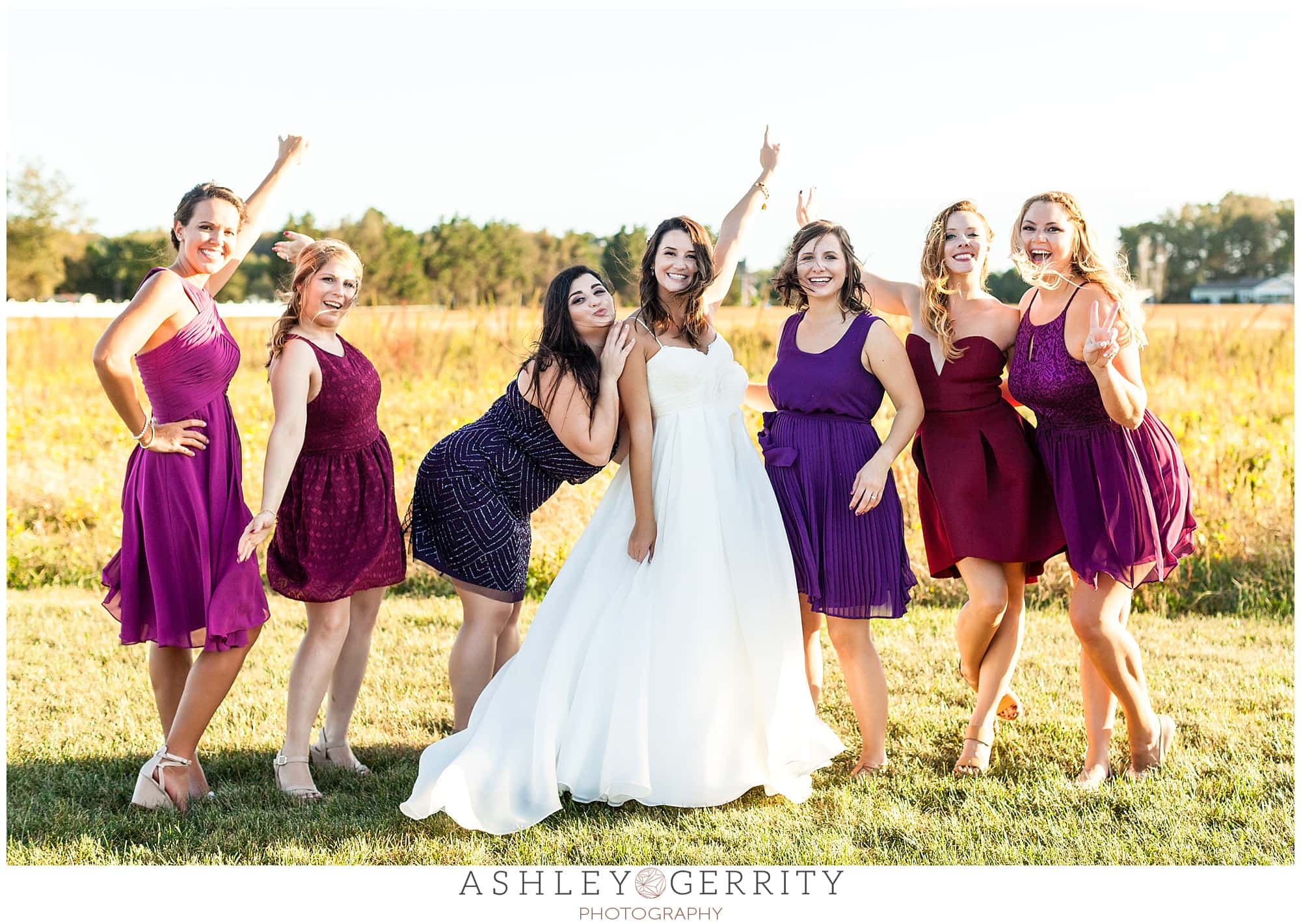 Celebratory bride posing with her wedding party dressed in short dresses in jewel tones