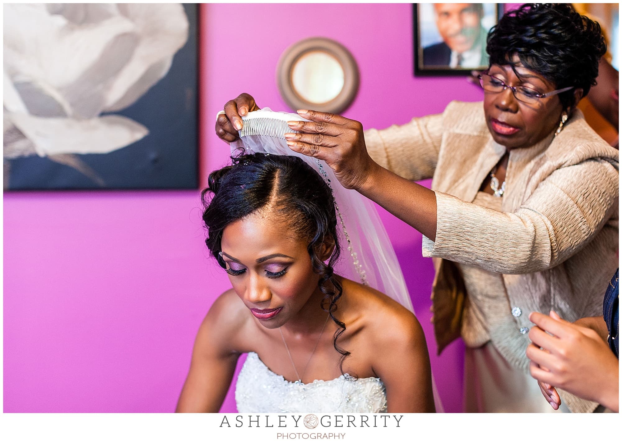 Bride's mother putting her veil on her in front of portrait of her late father.