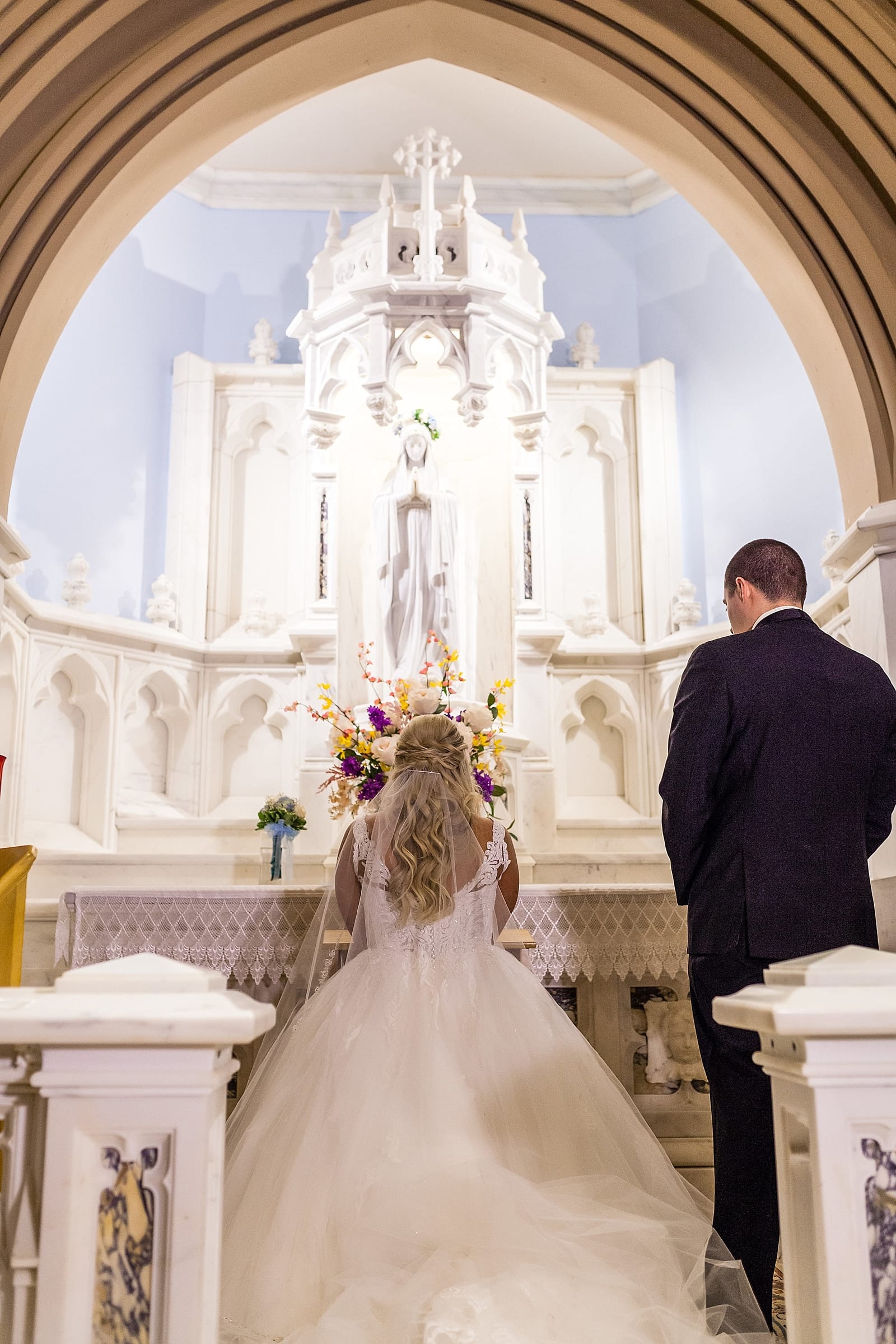 Bride kneels at the altar to the mother Mary during a catholic wedding mass at St Matthew's Church in Conshohocken.