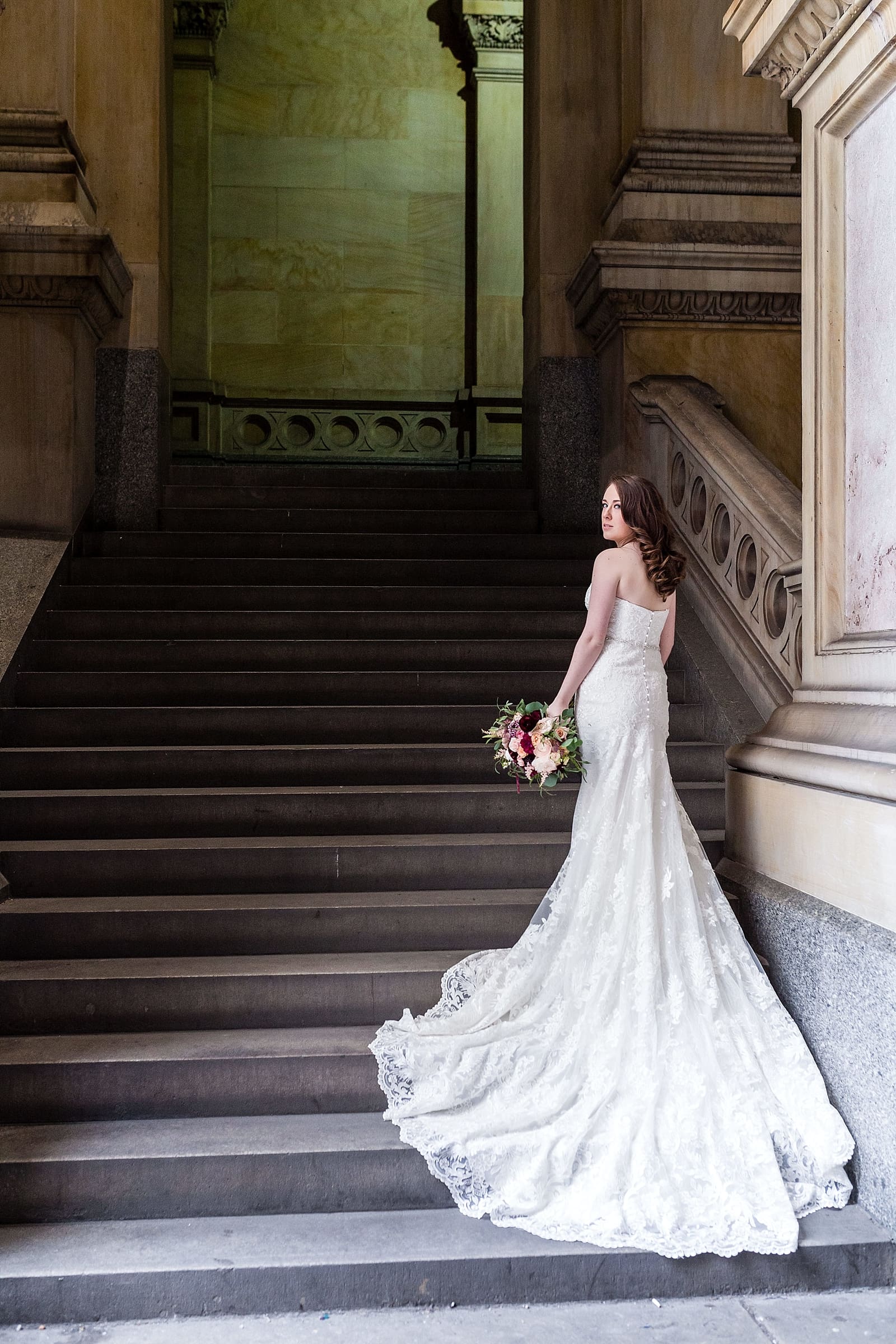 Dramatic bridal portrait from behind with long dress train and bouquet in the stairwell, college of physicians wedding