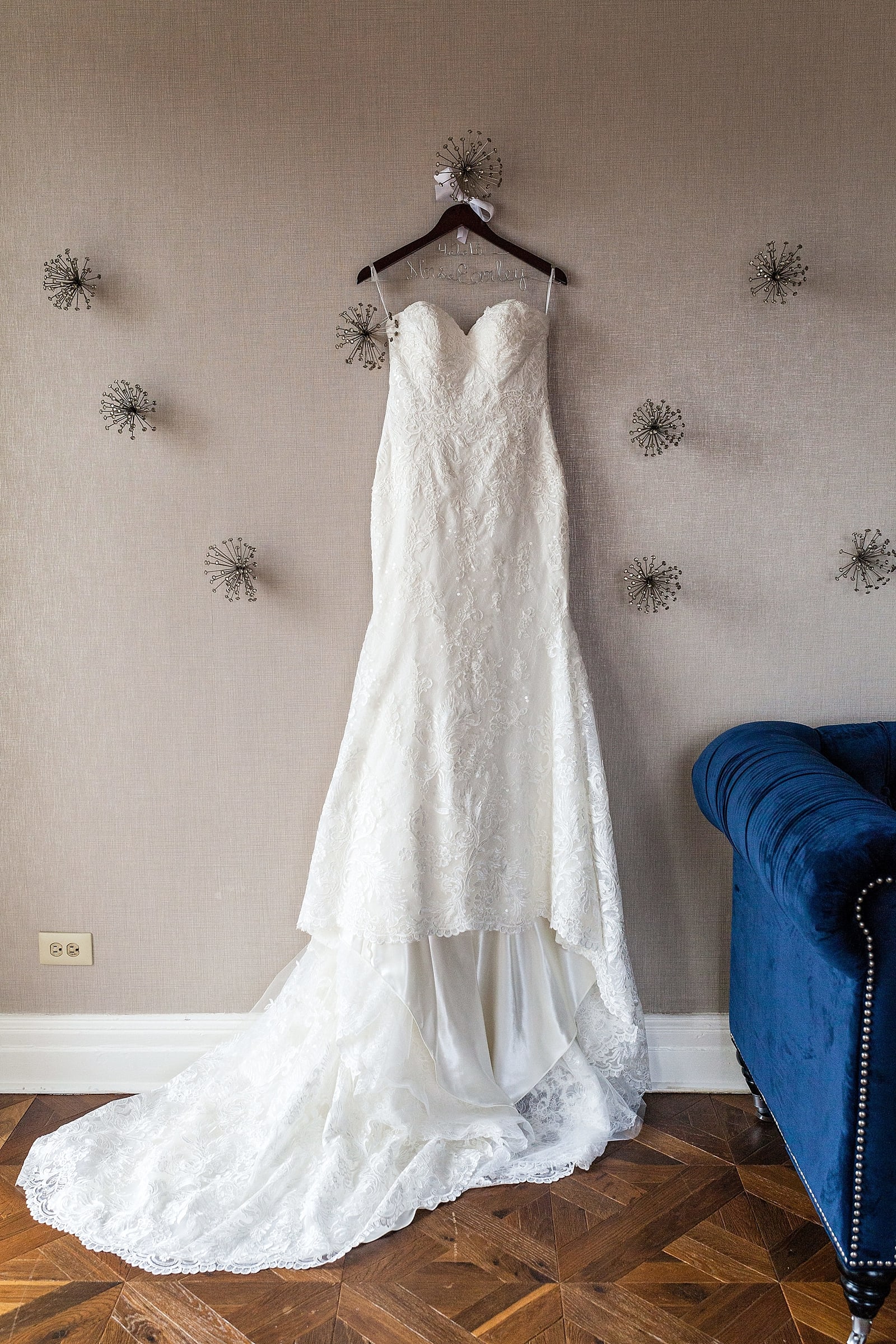Lace wedding dress hanging on detailed hanger with name and date before wedding