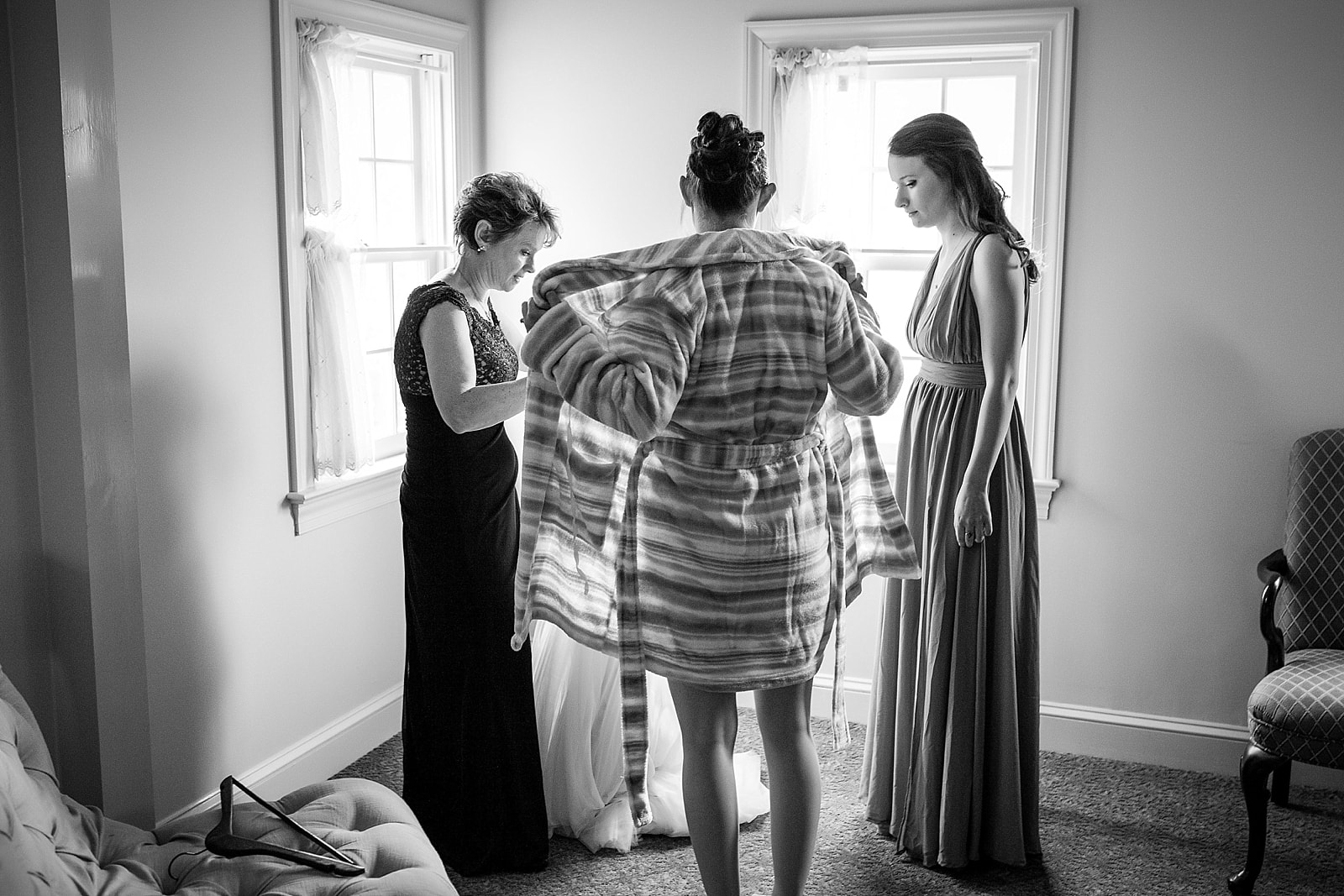 Bride about to out on her wedding dress with mother and bridesmaid