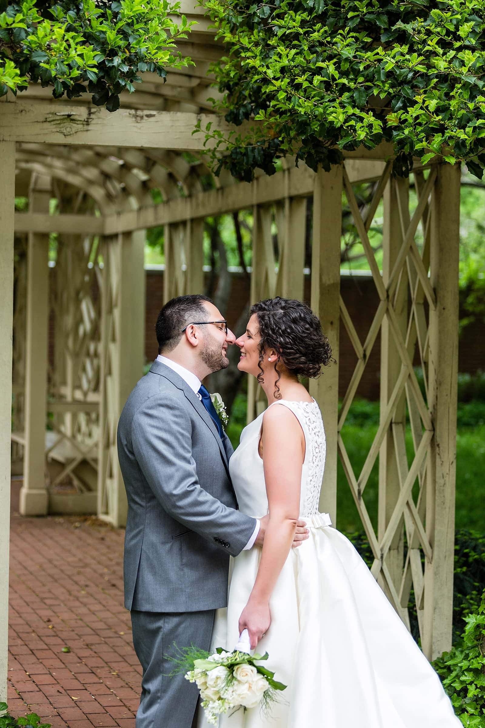 Bride in Pronovias & Groom in Grey Indochino suite embrace in Philadelphia's 18th Century Gardens