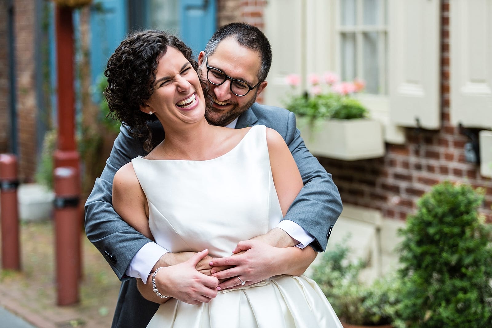 Groom embraces a laughing bride from behind in Philadelphia's Elfreth's Alley
