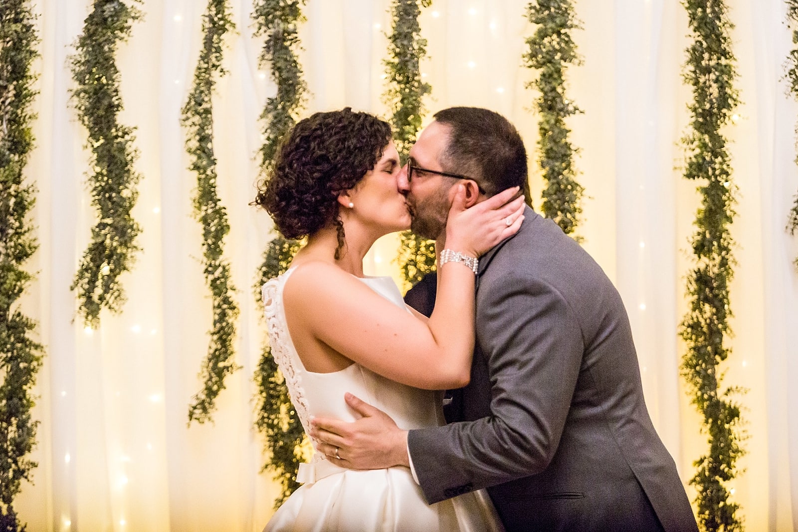 Bride & Groom first kiss in front of a hanging greenery wall for their ceremony backdrop at Richmond Hall