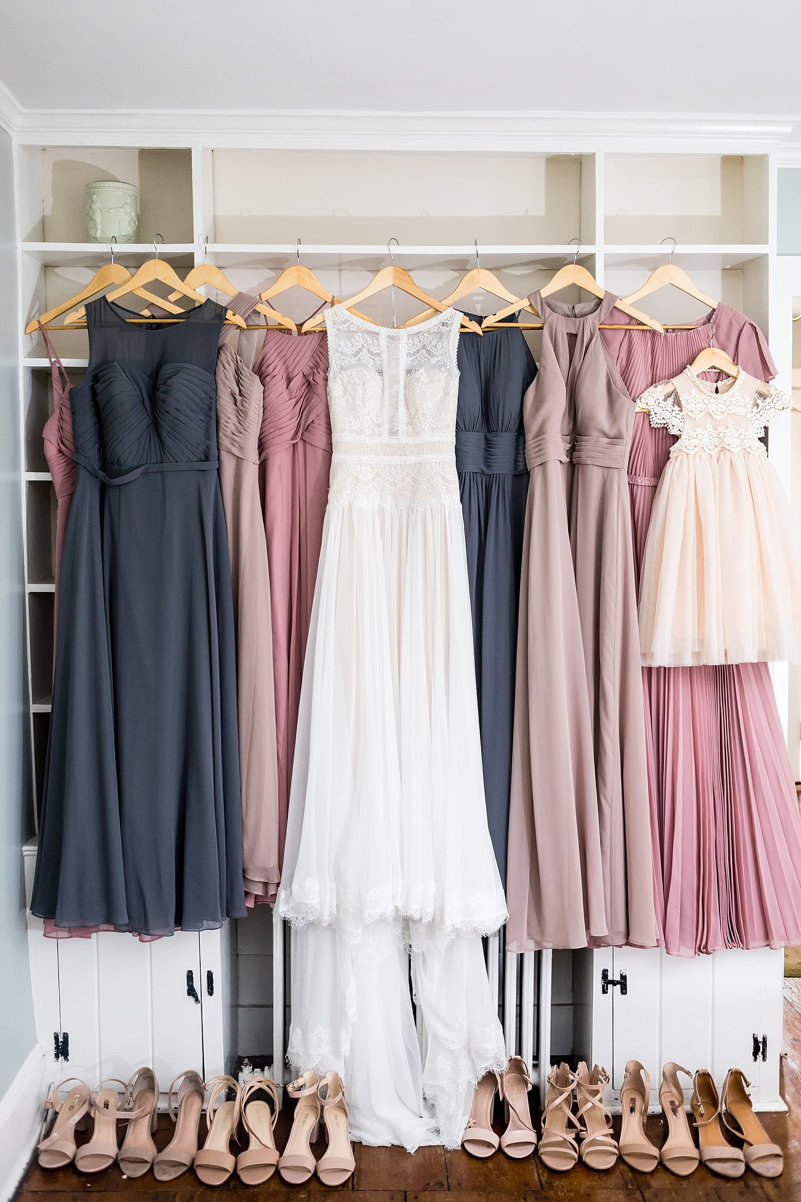 Mauve toned bridesmaid dresses hanging with a lace wedding dress.