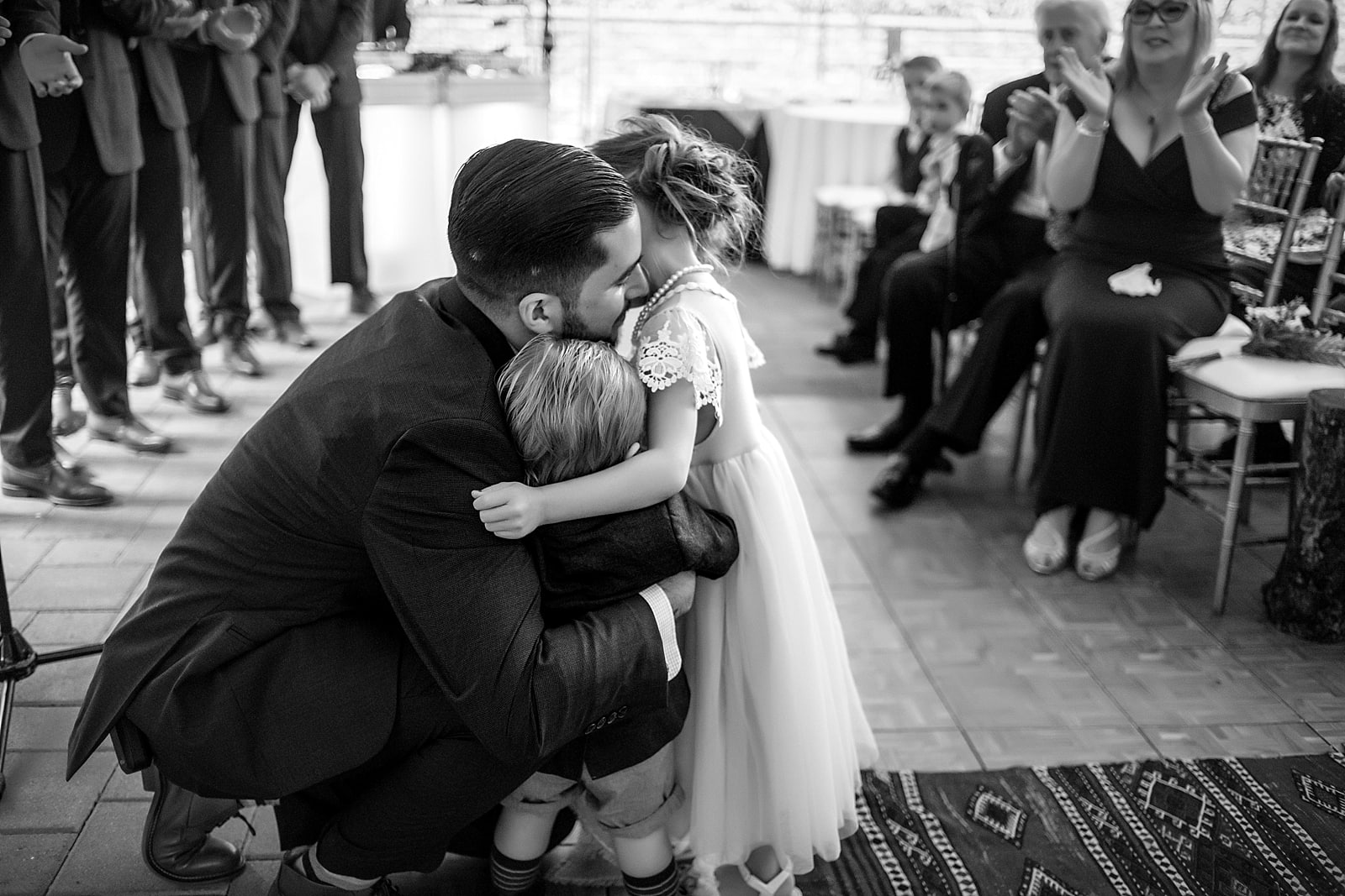 Groom embraces ring bearer and flower girl at the top of the aisle