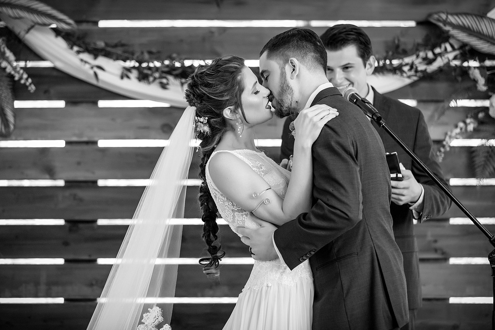 black and white photo of the bride & groom's first kiss in front of wooden shiplap ceremony backdrop