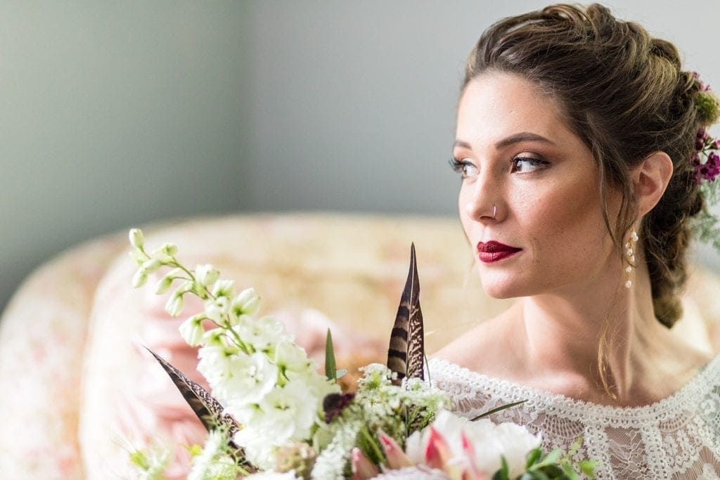 Window lit bridal portrait of bohemian tattooed bride with a textural wedding bouquet with feathers