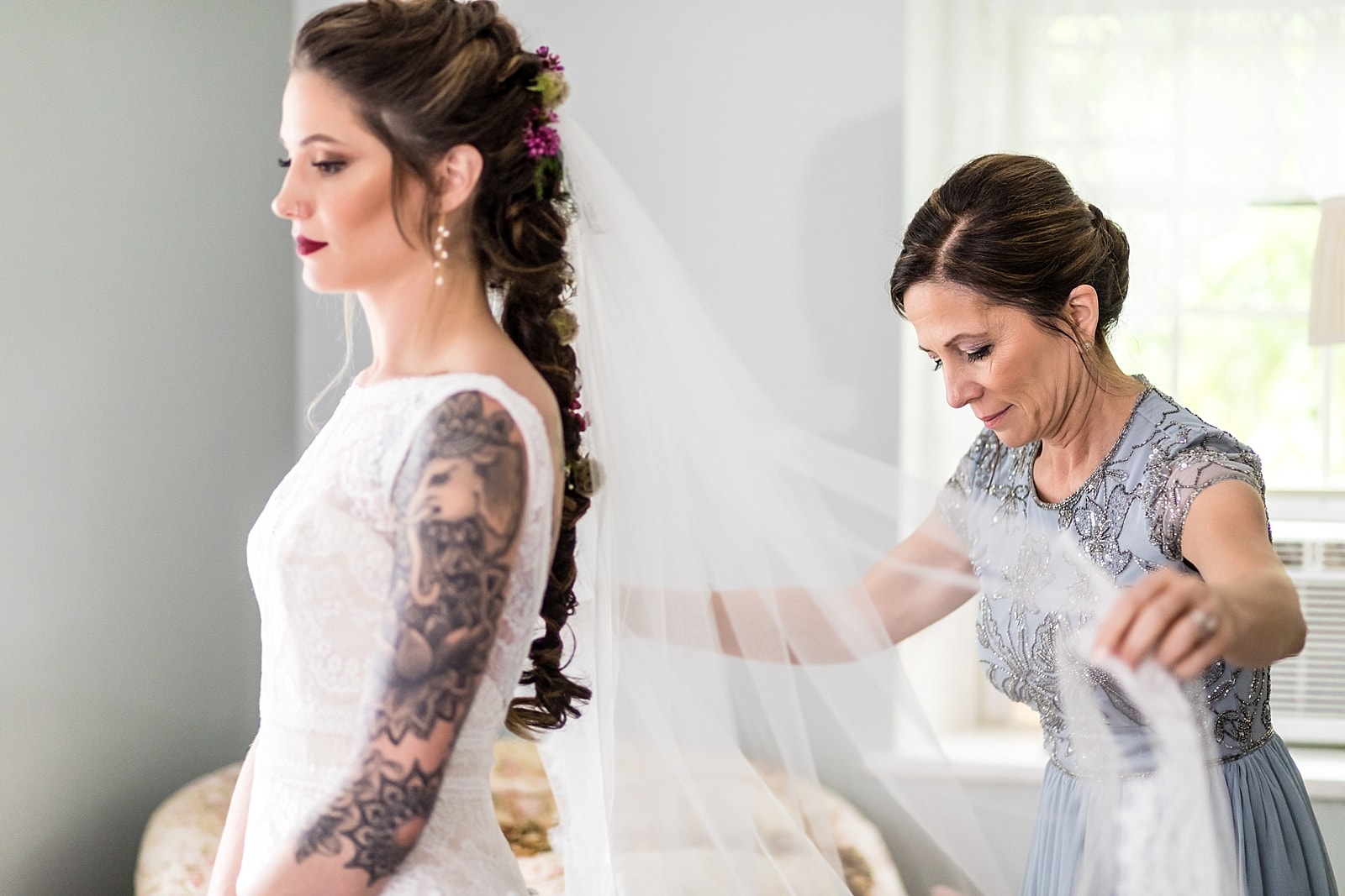 Mother putting the veil on a tattooed bride with wildflowers in her hair at the Inn at Millrace Pond