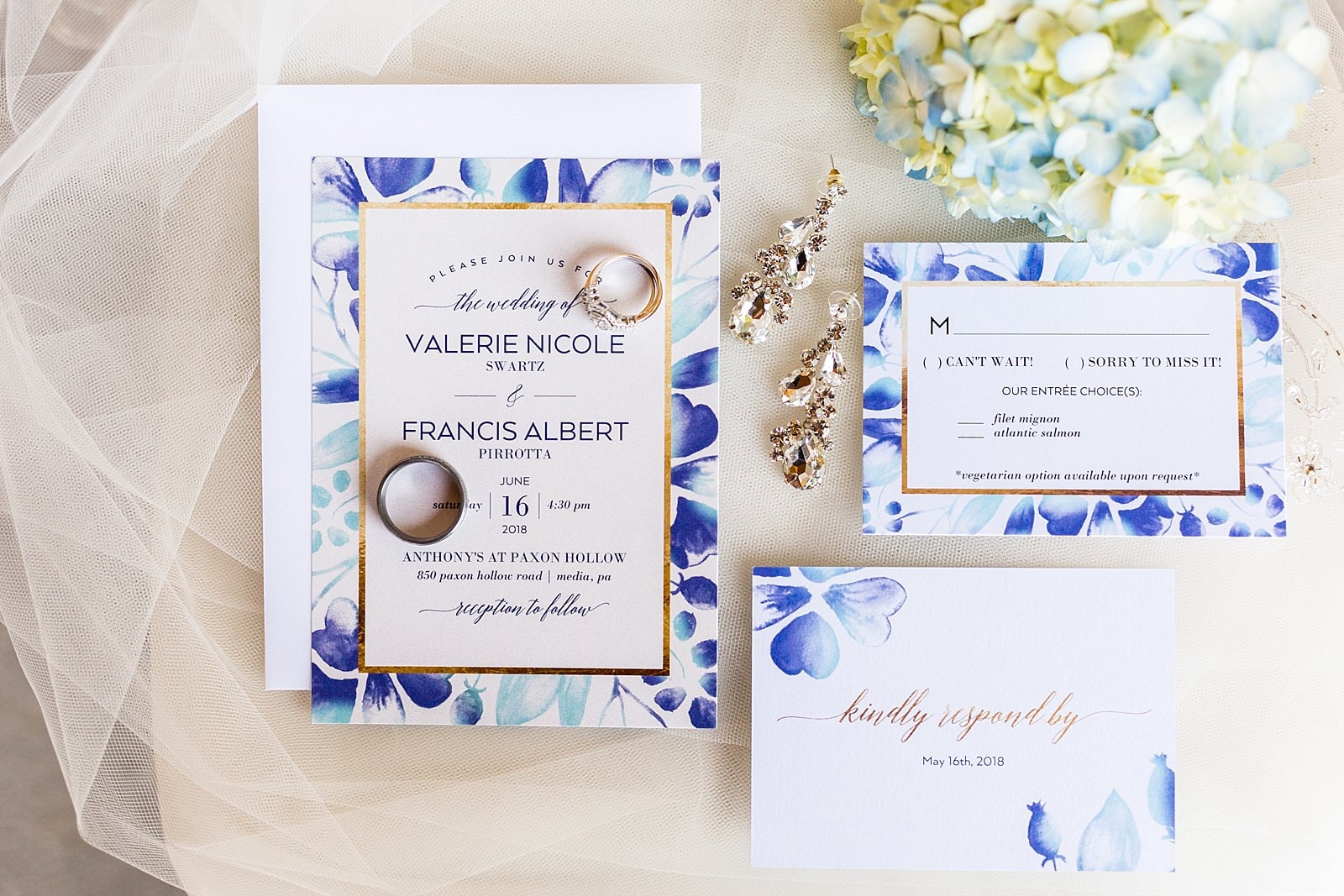 flat lay of blue floral invitation suite with bridal jewelry including heirloom style diamond engagement ring and wedding bands