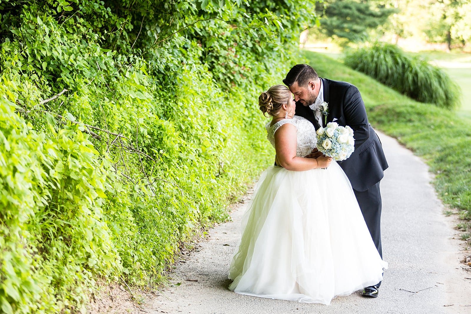 groom embraces bride in greenery at Anthony's at Paxon Hollow Country Club