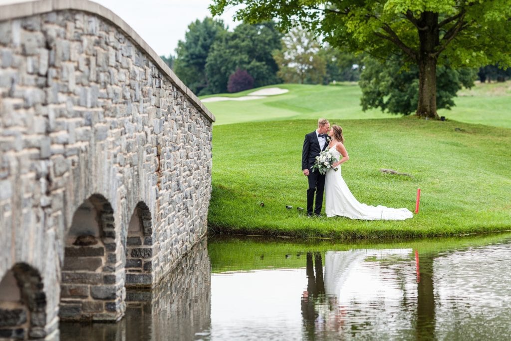 Bride & Groom kiss alongside a stone bridge and water feature on the golf course at their Chubb Conference Center wedding
