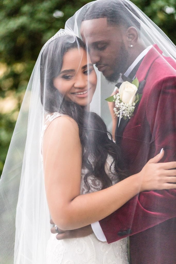 Bride & groom embrace under the veil as the sheer fabric waves in front of the camera.