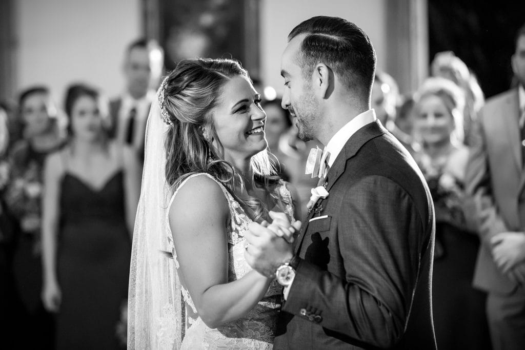 Bride & groom dance their first dance as their wedding guests look on. Photographed in black & white