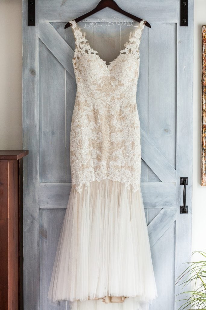 Lace trumpet style Watters wedding gown from the Bridal Garden hanging on the back of a grey painted barndoor