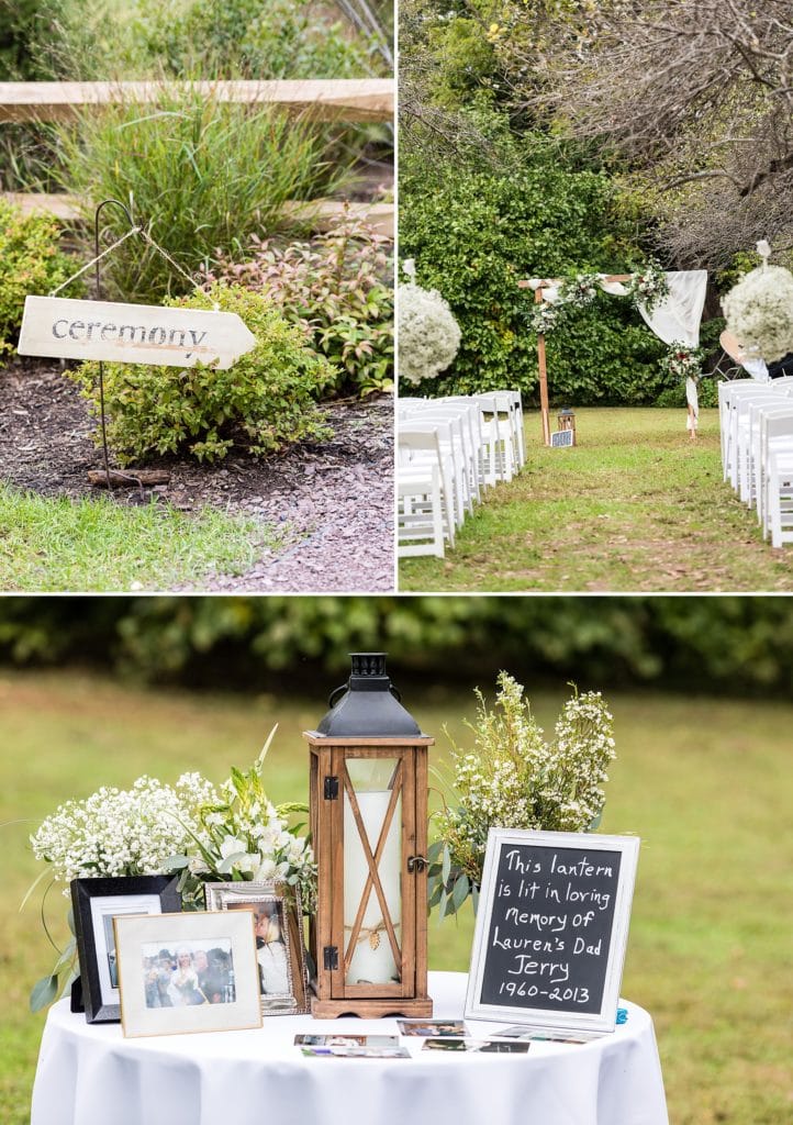 Wedding ceremony details for a John James Audubon Center wedding ceremony include a ceremony arch draped with fabric and roses, a wooden ceremony sign, and a memory table with chalk signs