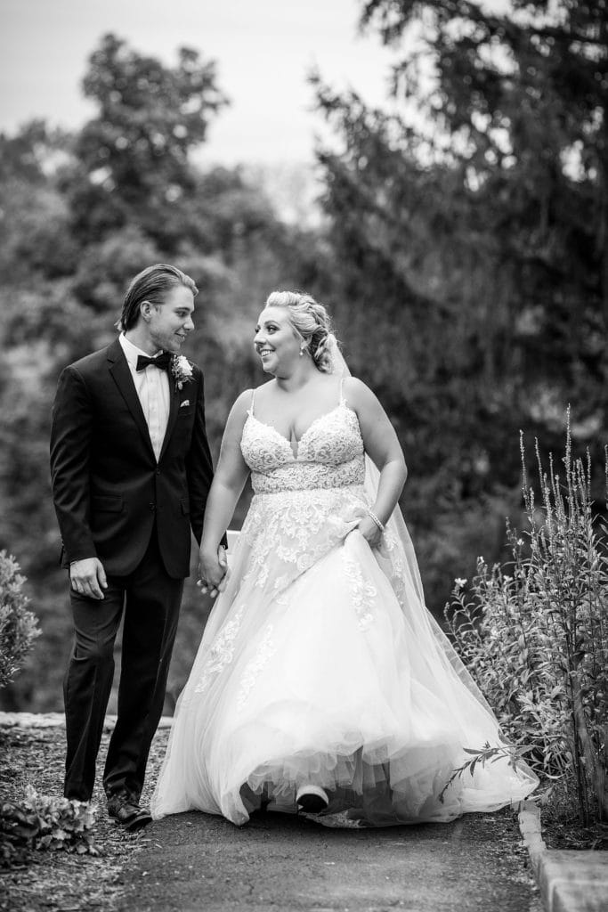 Bride & groom laugh together while walking hand in hand for a wedding photo at their John James Audubon Center wedding. Photographed in black & white