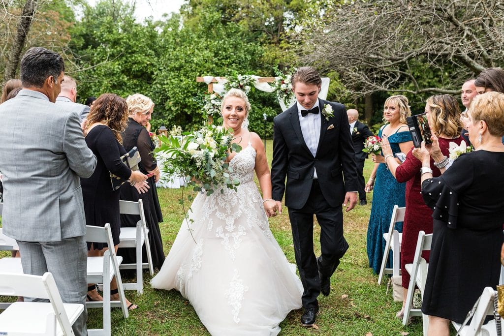 Bride carrying cascading greenery bouquet recesses from her wedding ceremony at the J. J. Audubon center with her groom in hand