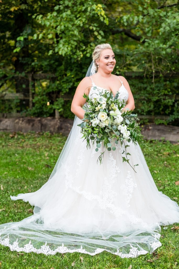 Bride smiles for a portrait as she holds a cascading bouquet of roses and greenery