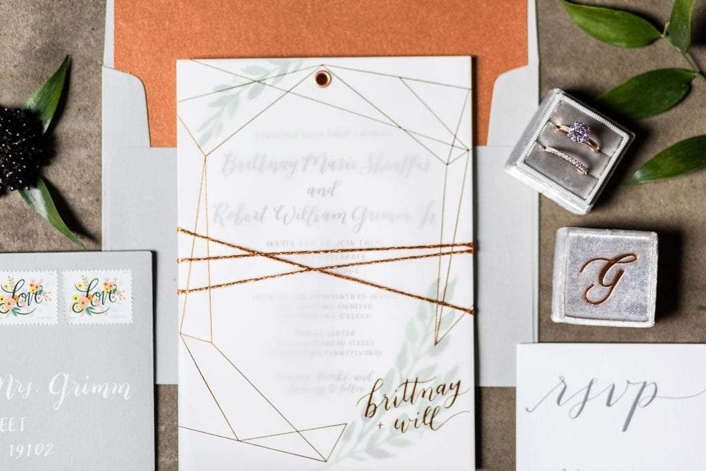 Copper & Grey wedding invitation by Hello Bird styled against concrete with loose greenery paired with custom wedding bands from L Priori in a monogrammed Mrs Box