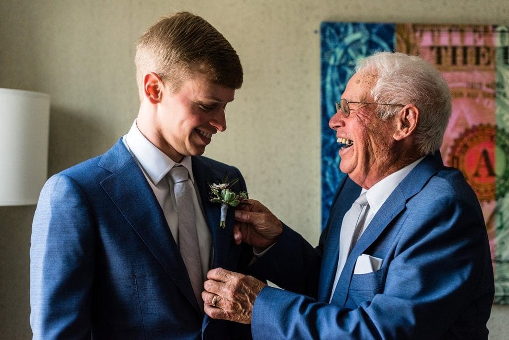 Groom's grandfather and best man puts his boutonnierre on him as he gets ready for his wedding day