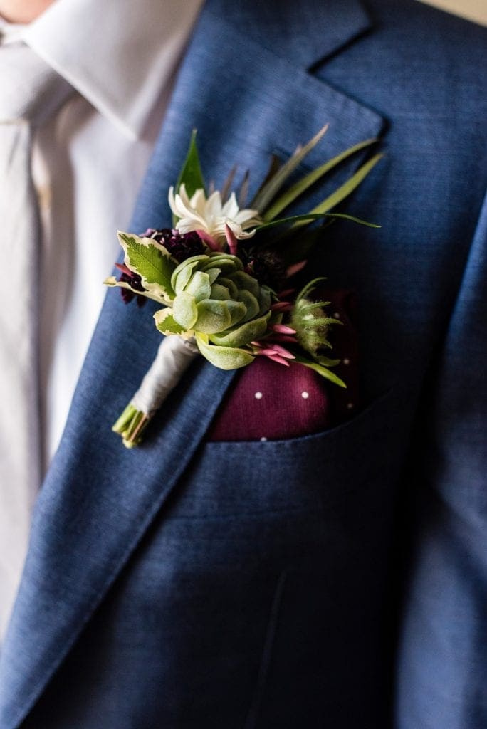 Succulent boutonnierre by Devon & Pinket against a blue tailored groom's suit and burgundy polka dotted handkerchief