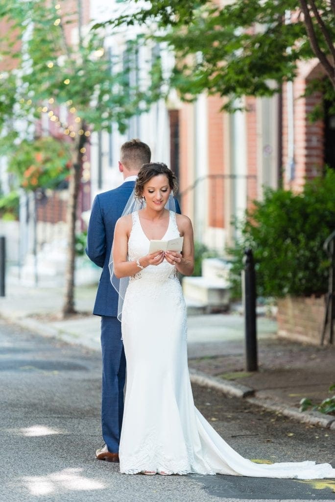 Bride & groom reading letters they had written for each other while standing back to back before their first look on Addison St in Philadelphia