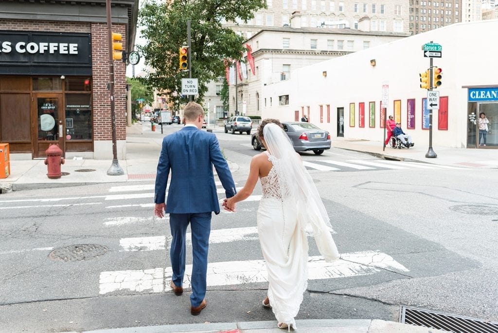 Bride & Groom walk hand in hand across Spruce St in Philadelphia on their way to their wedding party photos before their Kimmel Center Wedding