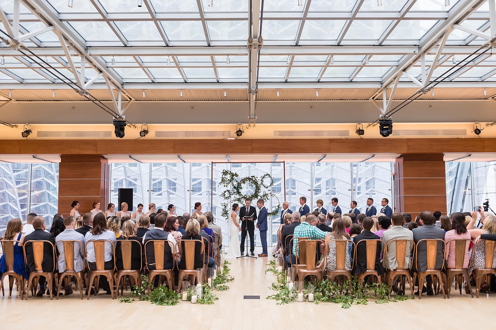 Wide photo of the industrial ceremony space for Kimmel Center wedding showing a ceremony backdrop of copper pipe and greenery wreaths