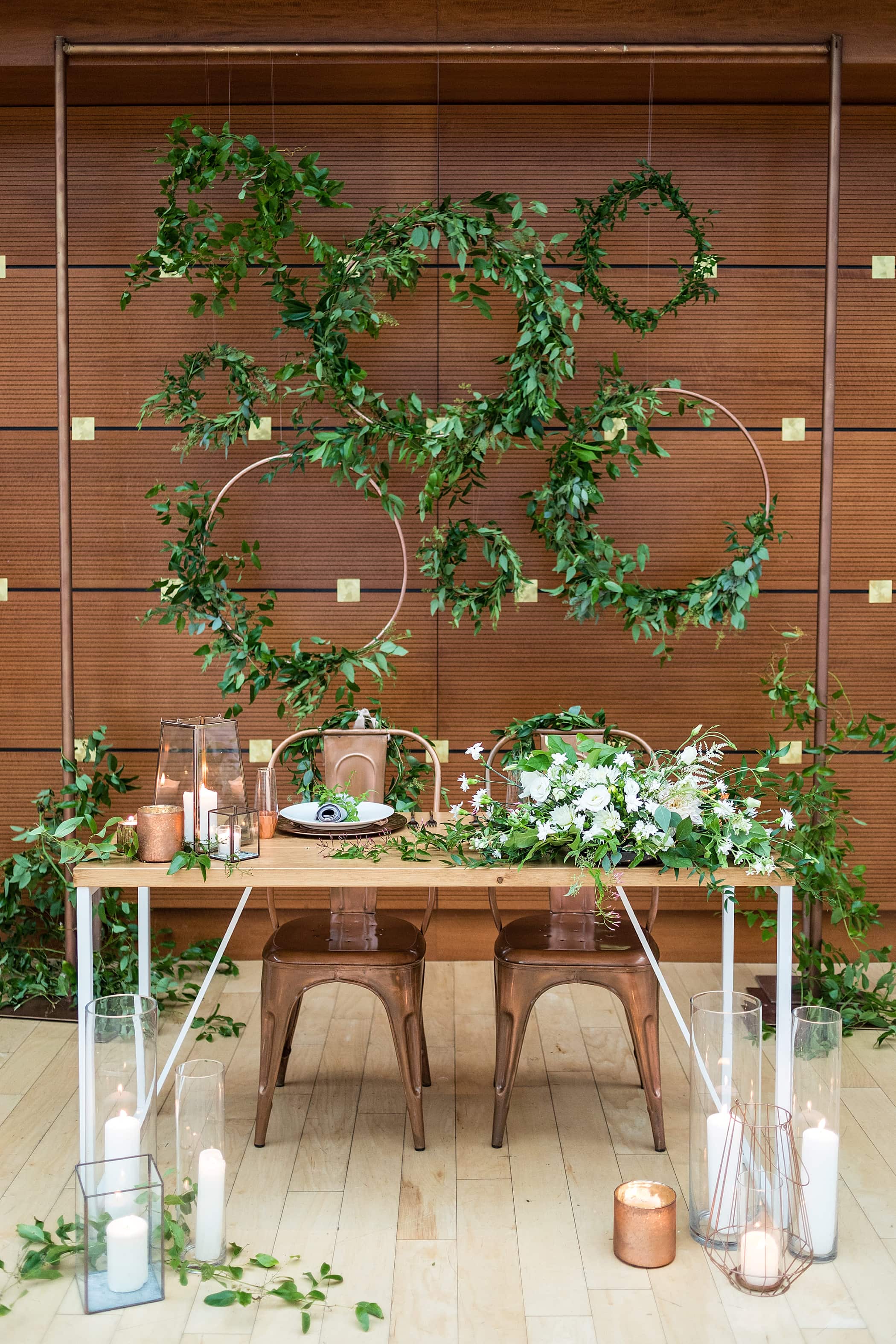 Sweetheart table against the wooden walls of the Kimmel Center with wreaths of copper piping and loose greenery
