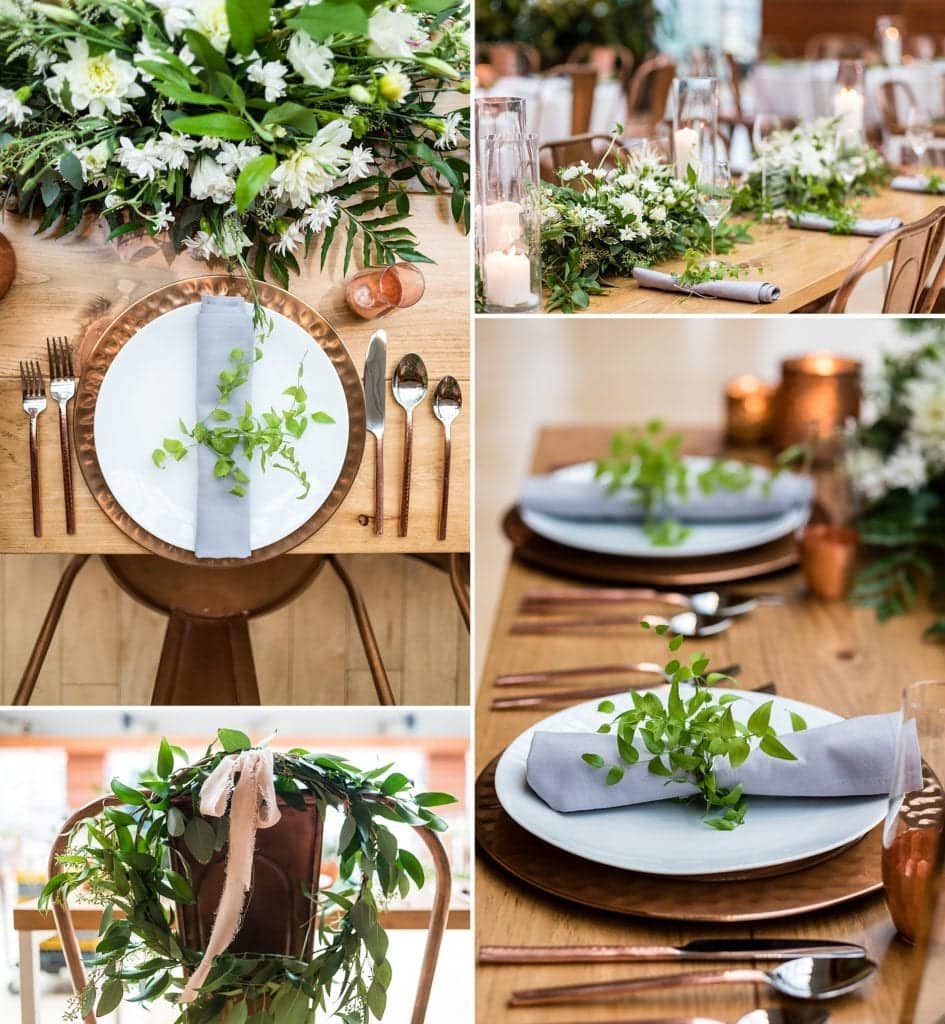 Place settings for a wedding with copper chargers and copper utensils, light grey napkins tied in greenery