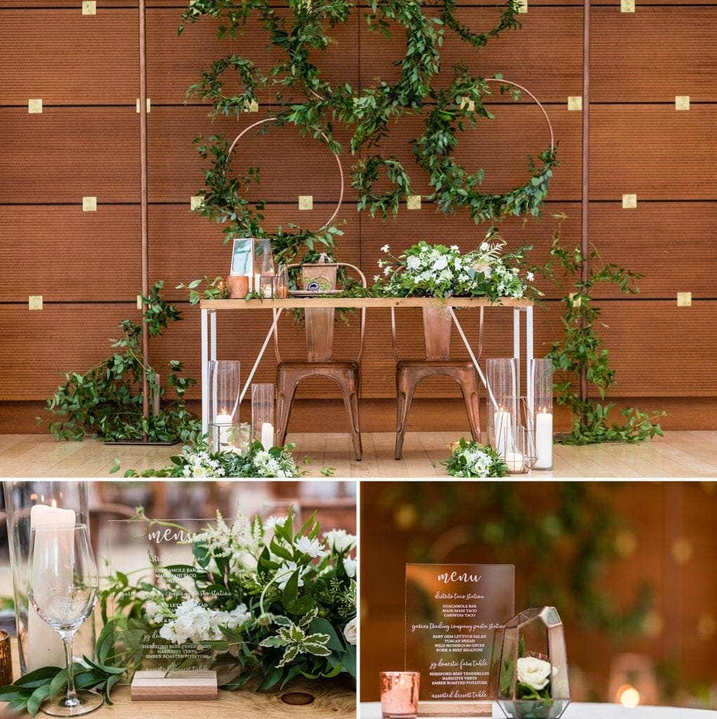 Sweetheart table against the wooden walls of the Kimmel Center with wreaths of copper piping and loose greenery with menus printed on acrylic