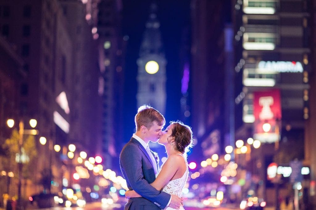 Black & white wedding photo of a bride & groom on Broad St in Philadelphia in front of City Hall as traffic rushes by