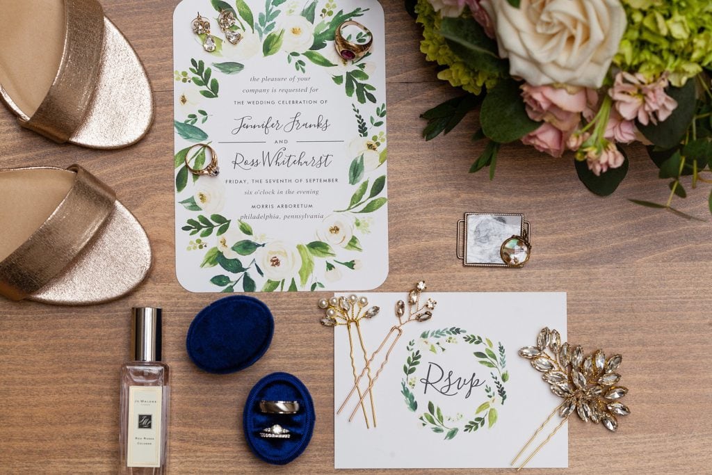 Flat lay of custom wedding hair pins, Jo Molone purfume and a greenery inspired wedding invitation