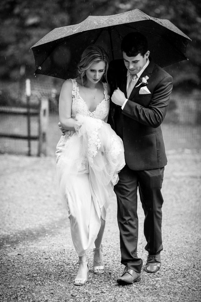 Bride & groom walk together under an umbrella during their Morris Arboretum wedding, rainy wedding portraits