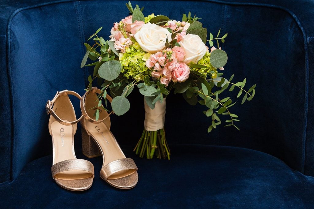 Gold Chinese Laundry wedding shoes and loose floral bouquet against a blue velvet chair.