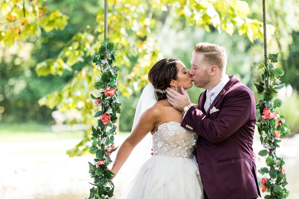 bride & groom kissing on a floral swing