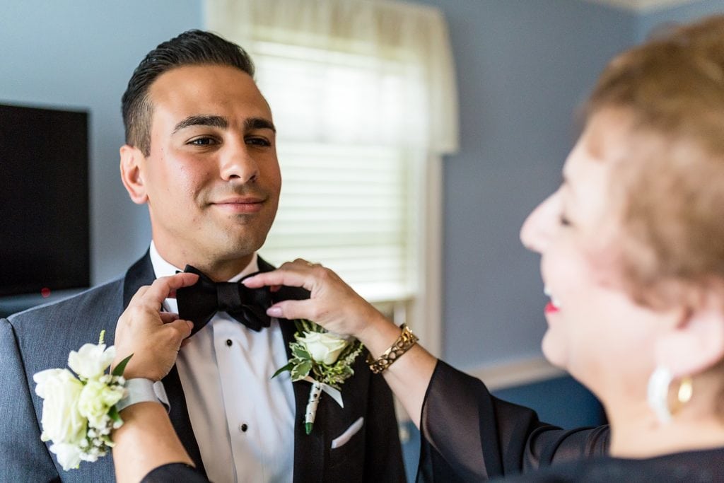 Mother ties a bowtie on her son, the groom
