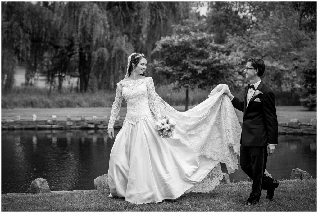 black and white outdoor portrait of bride and groom walking together while groom is carrying the brides train