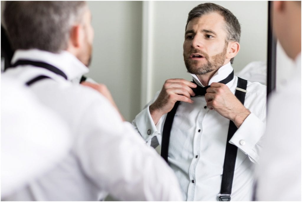 Groom adjusting his bowtie in the mirror