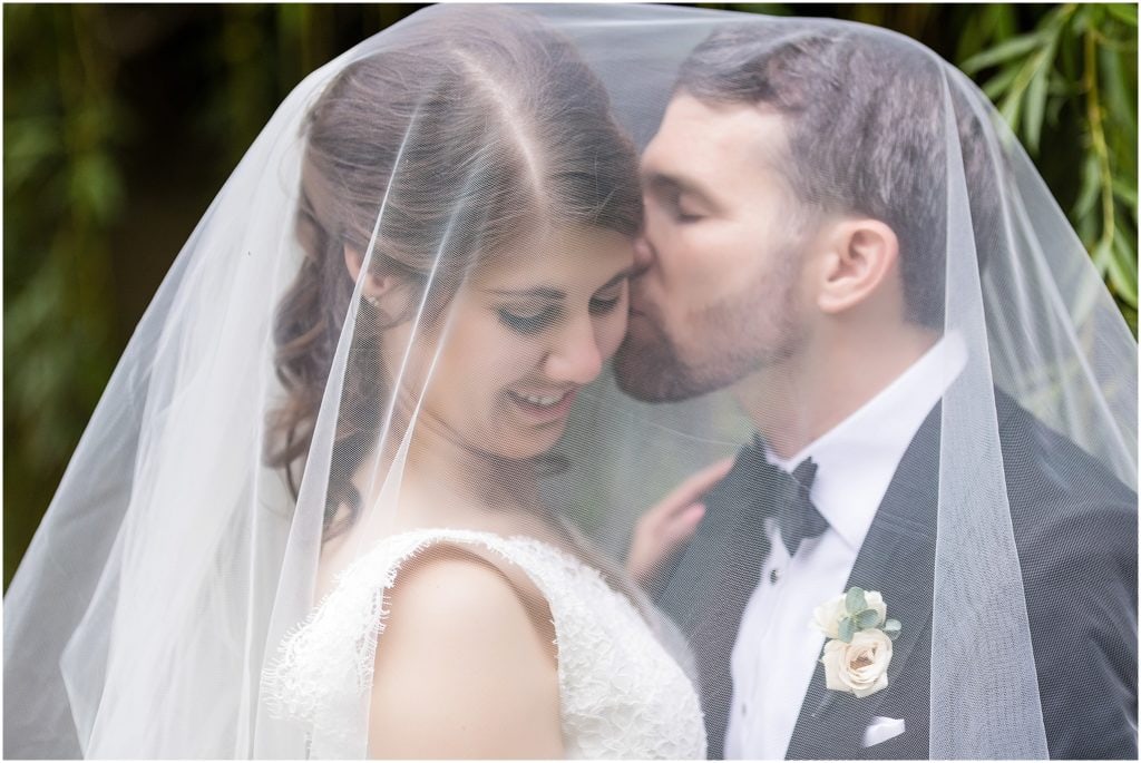 groom kissing brides cheek under her veil